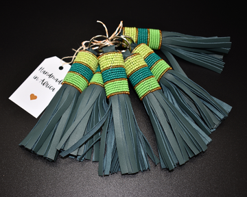 A leather key holder with green  tassels and Maasai beadwork, displayed against a dark background with a 'Handmade in Kenya' tag.